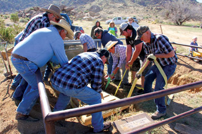 A crew of northeast Clark County residents lower a concrete vault lid down into the Gold Butte grave of Arthur Coleman who was originally buried there in 1958. Coleman’s remains were returned to the site on Saturday after the grave was vandalized in the spring of 2014.  PHOTO BY VERNON ROBISON/Moapa Valley Progress.