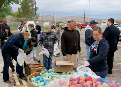 Volunteers hustle to pack produce and other food items into bags for distribution as cars line up in the background to pick up the food at a Mobile Food Pantry held at Grant Bowler Elementary School parking lot on Saturday morning. PHOTO BY VERNON ROBISON/Moapa Valley Progress.
